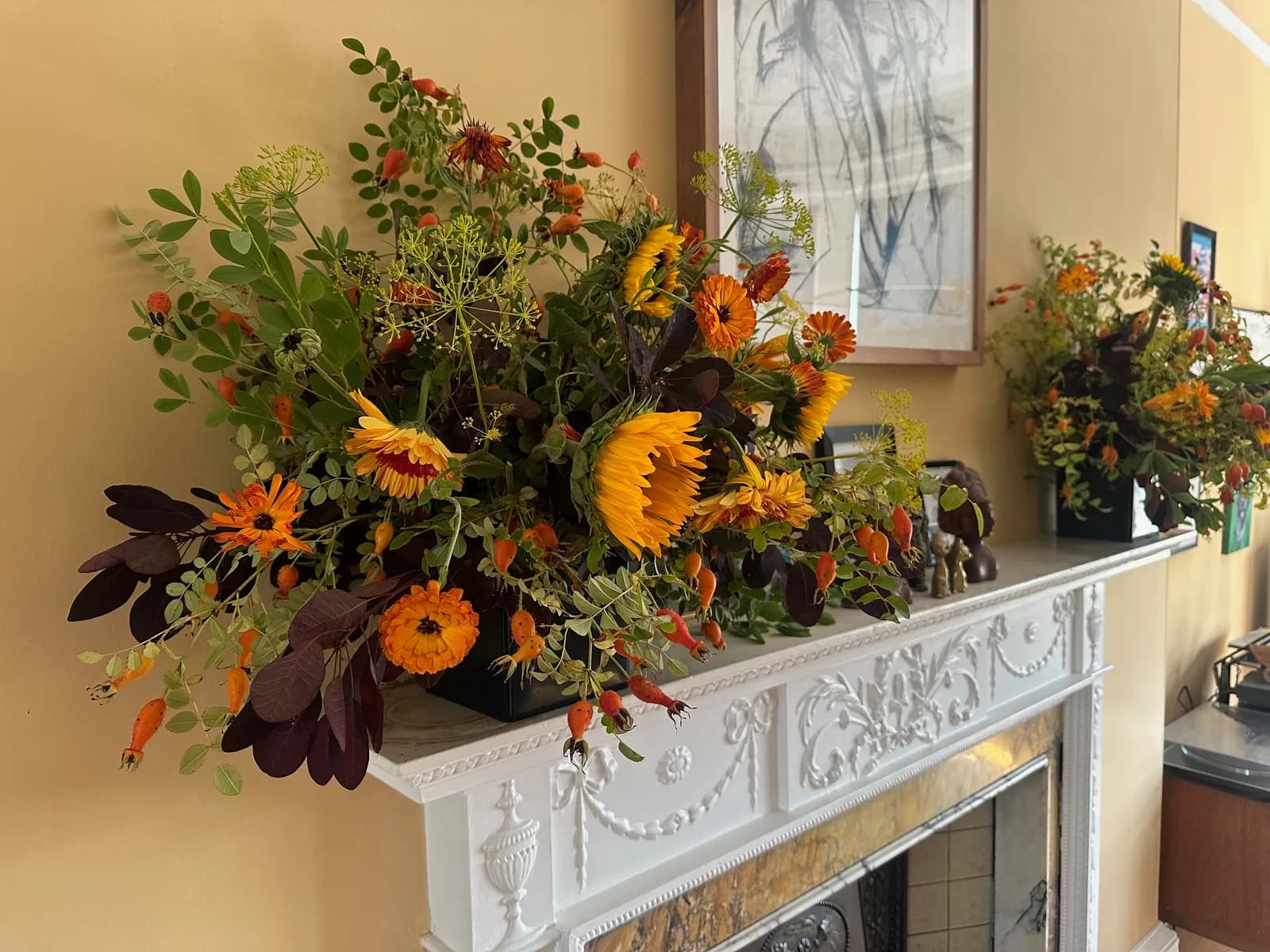 Sunflowers, foliage and colourful flowers arranged across a carved white mantelpiece