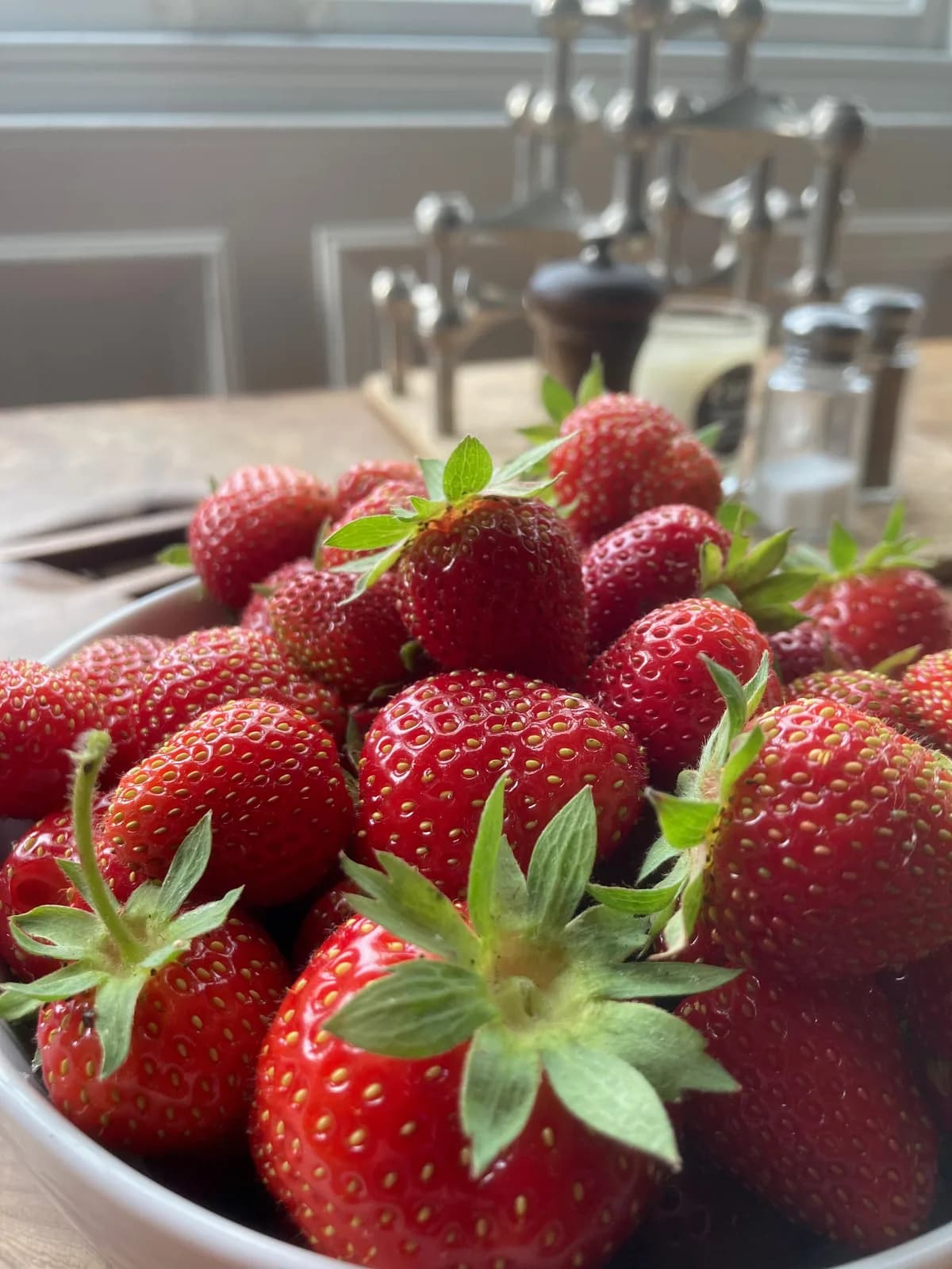 A white bowl heaped with ripe red strawberries on the dining table